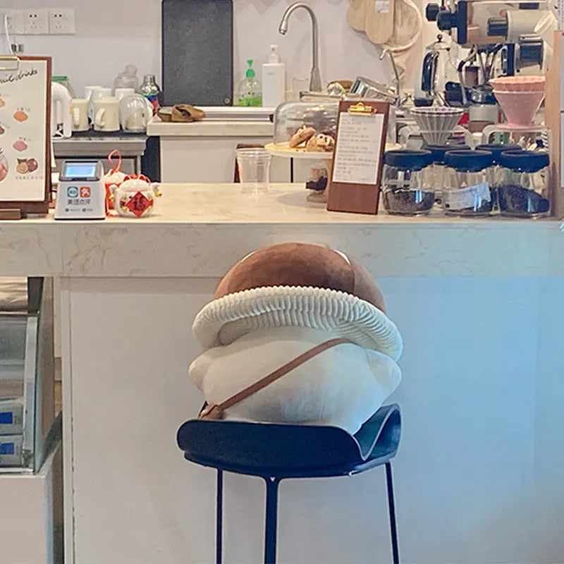 Pilz kuscheltier sitzt auf einem Stuhl im Cafe, dekoratives Plueschspielzeug im Alltag